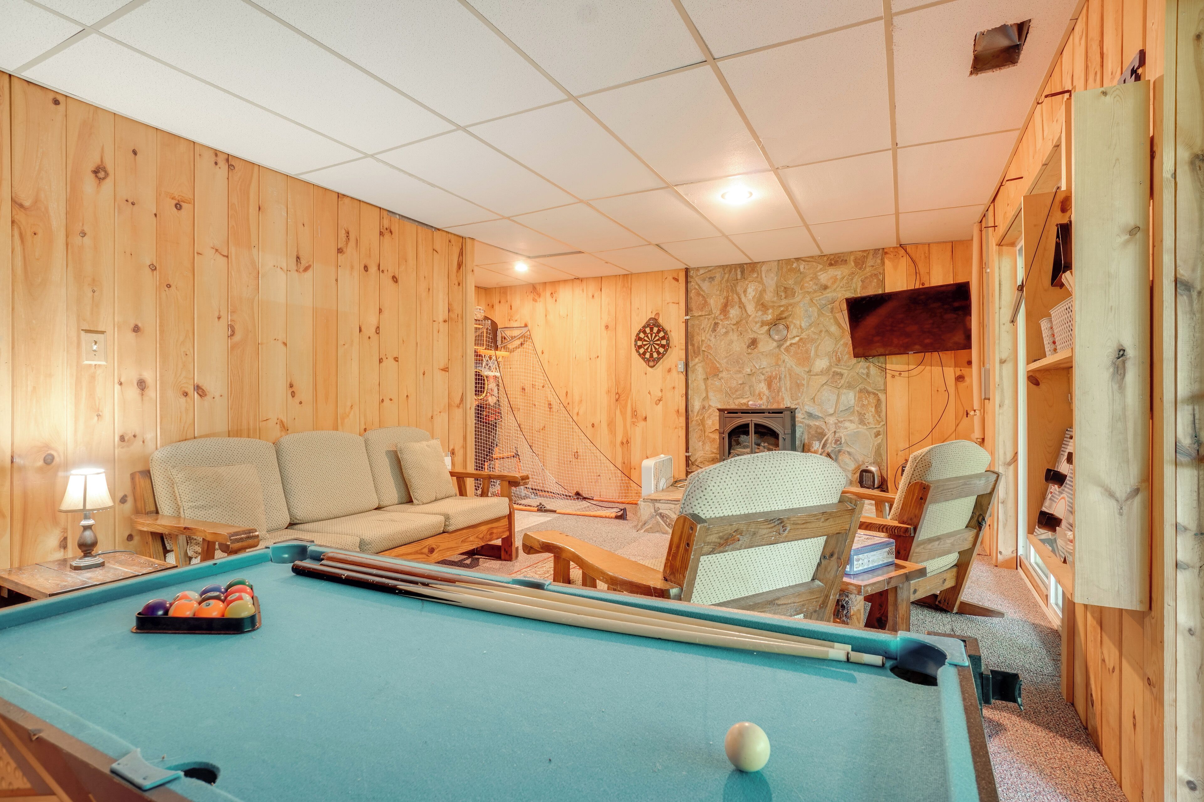 Ein Billardtisch mit blauer Spielvliesdecke, umgeben von Holzwänden und einer Wand aus Stein. Im Raum befinden sich zwei Sofas und zwei Sessel.