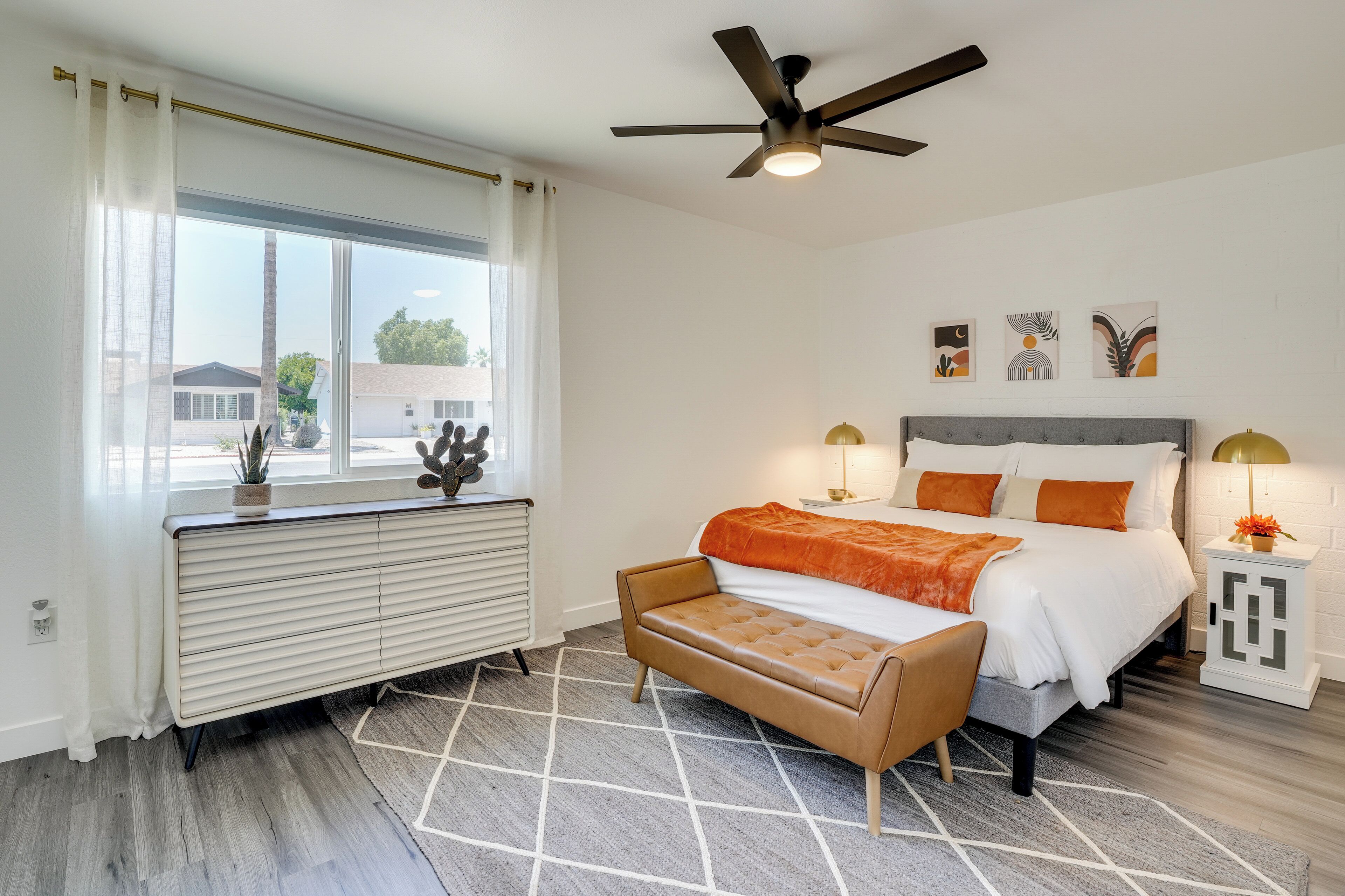 A modern bedroom with a bed, a bench, a radiator, a ceiling fan, and artwork on the wall.