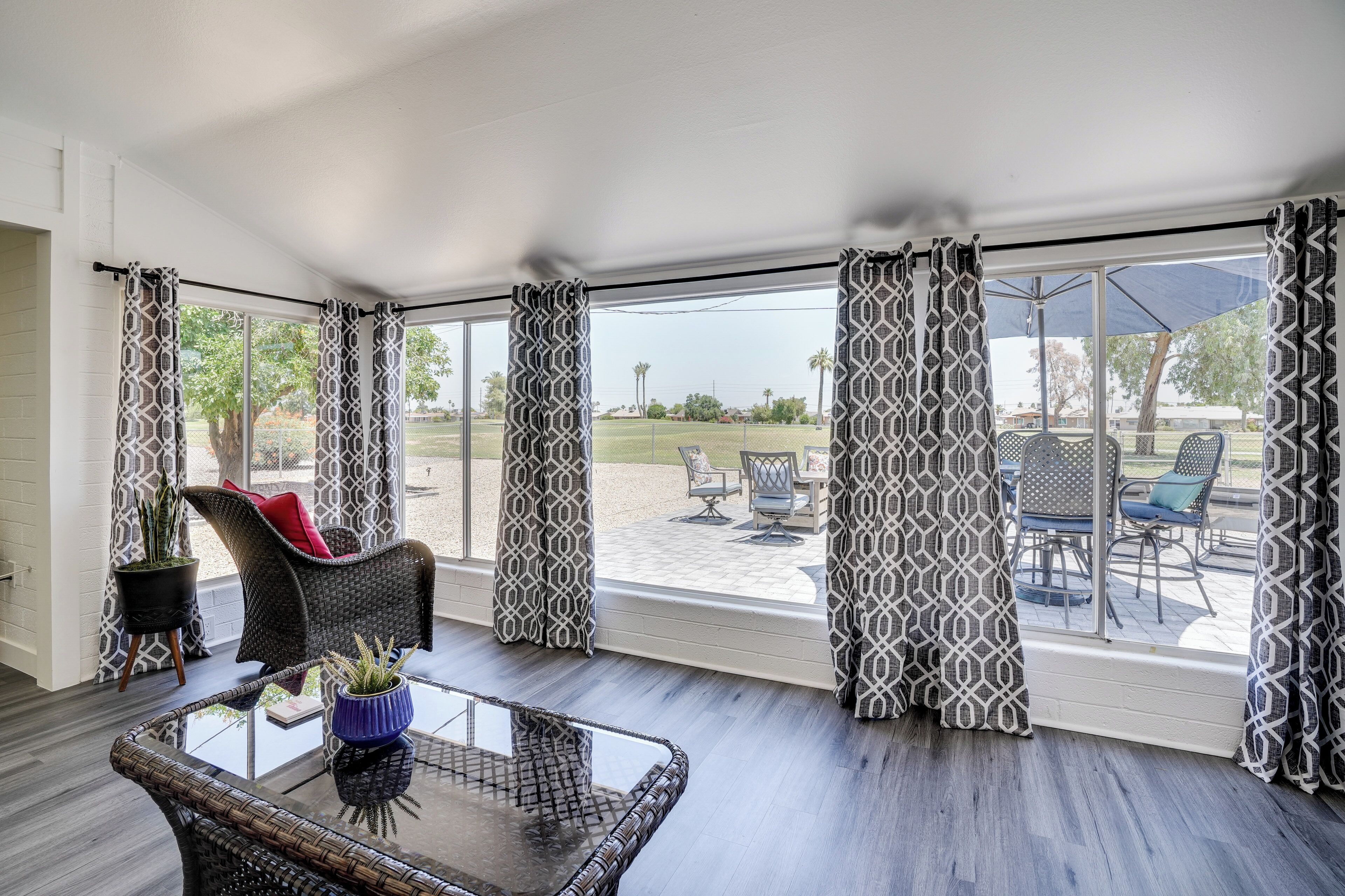 A room with a glass table, wicker chairs, and a view of an outdoor patio with furniture.