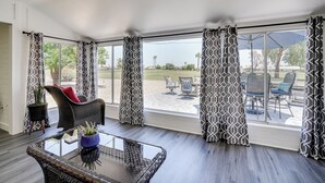 Une pièce avec une table en verre, des chaises en osier et une vue sur un patio extérieur aménagé avec du mobilier.