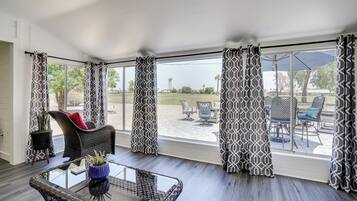 A room with a glass table, wicker chairs, and a view of an outdoor patio with furniture.