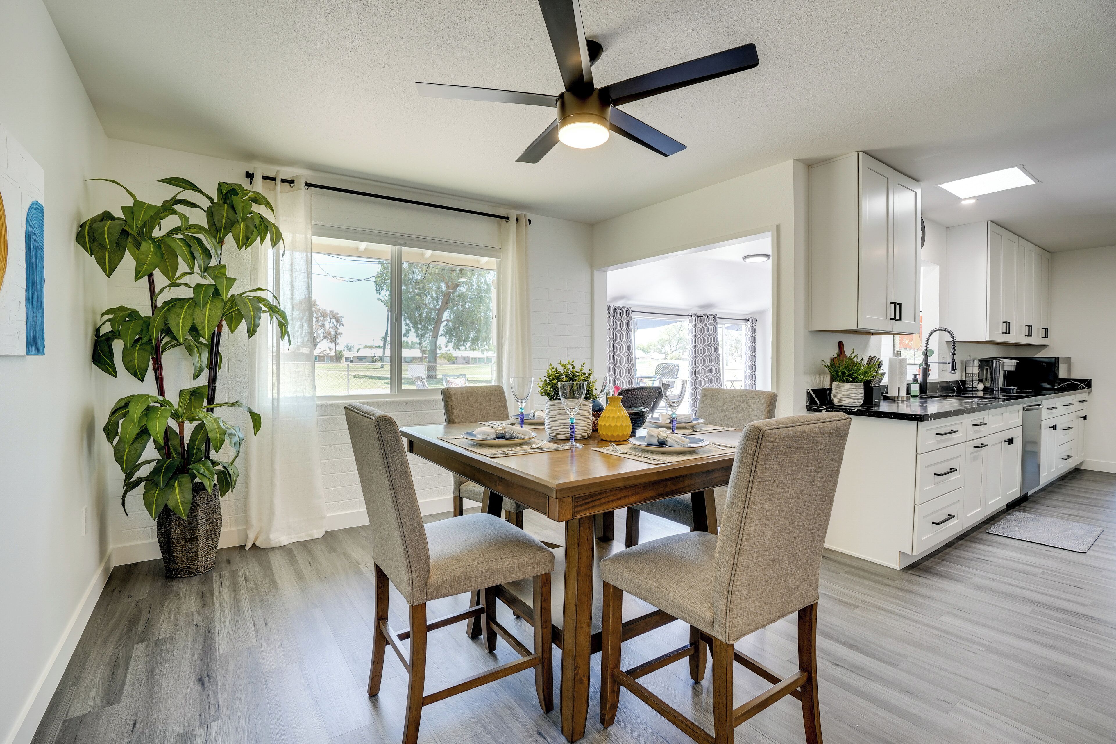 A modern kitchen with white cabinets, a dining table set for four, and a ceiling fan.