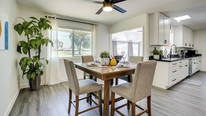 Une cuisine moderne avec des meubles blancs, une table à manger pour quatre personnes et un ventilateur de plafond.