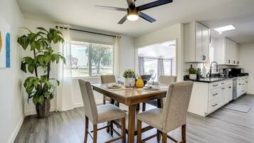 A modern kitchen with white cabinets, a dining table set for four, and a ceiling fan.