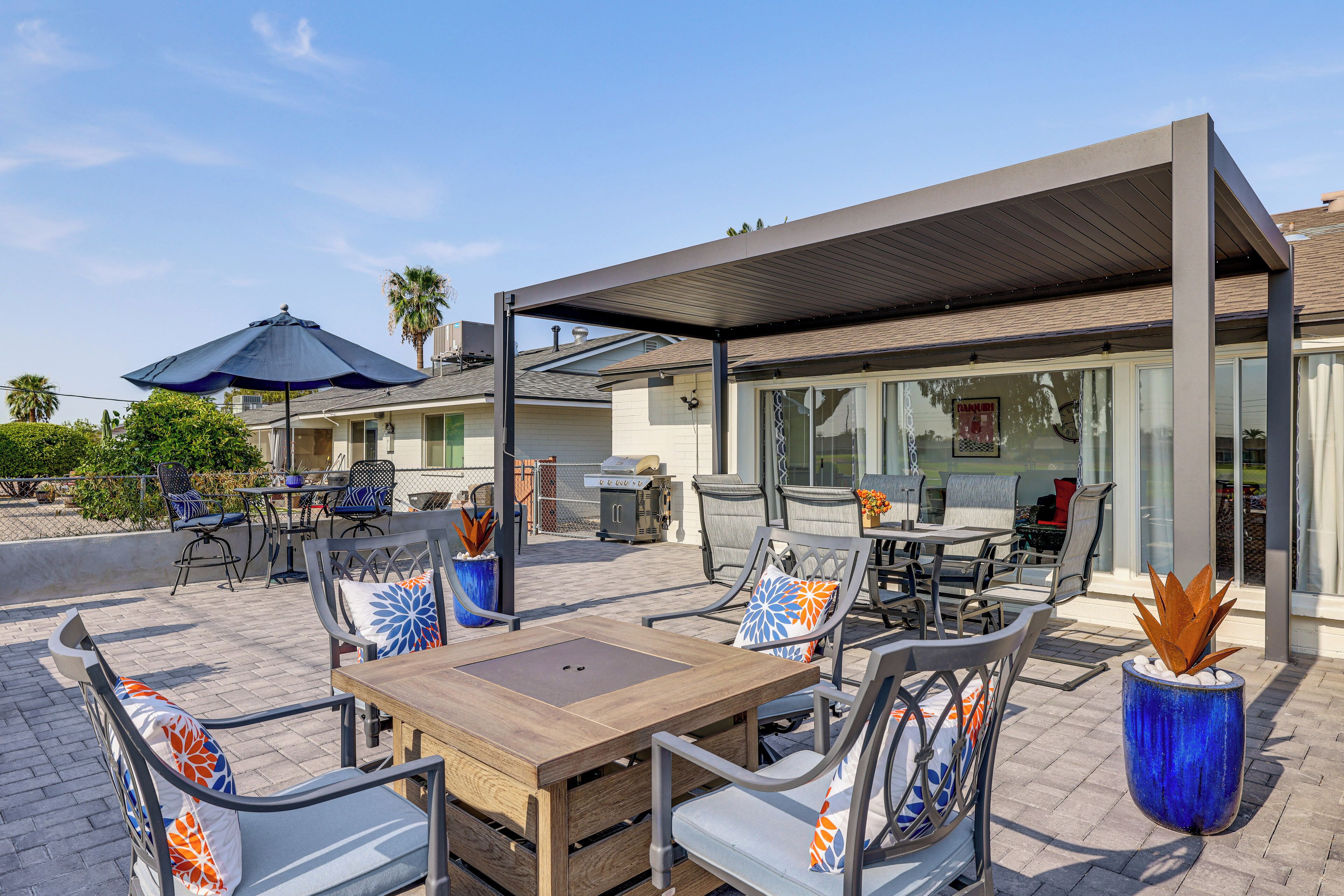 An outdoor patio area with a covered seating arrangement, a grill, and a poolside table.
