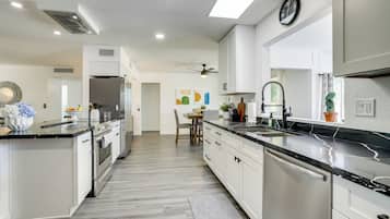 A modern kitchen with white cabinetry, stainless steel appliances, and a black marble countertop.