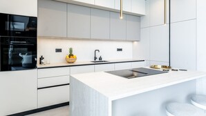 A modern kitchen with white cabinetry, a built-in oven, a stainless steel sink, and a central island with a black countertop. - Villa Belvedere 1 Zadarvillas (Sveti Filip i Jakov)