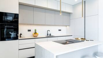 A modern kitchen with white cabinetry, a built-in oven, a stainless steel sink, and a central island with a black countertop.
