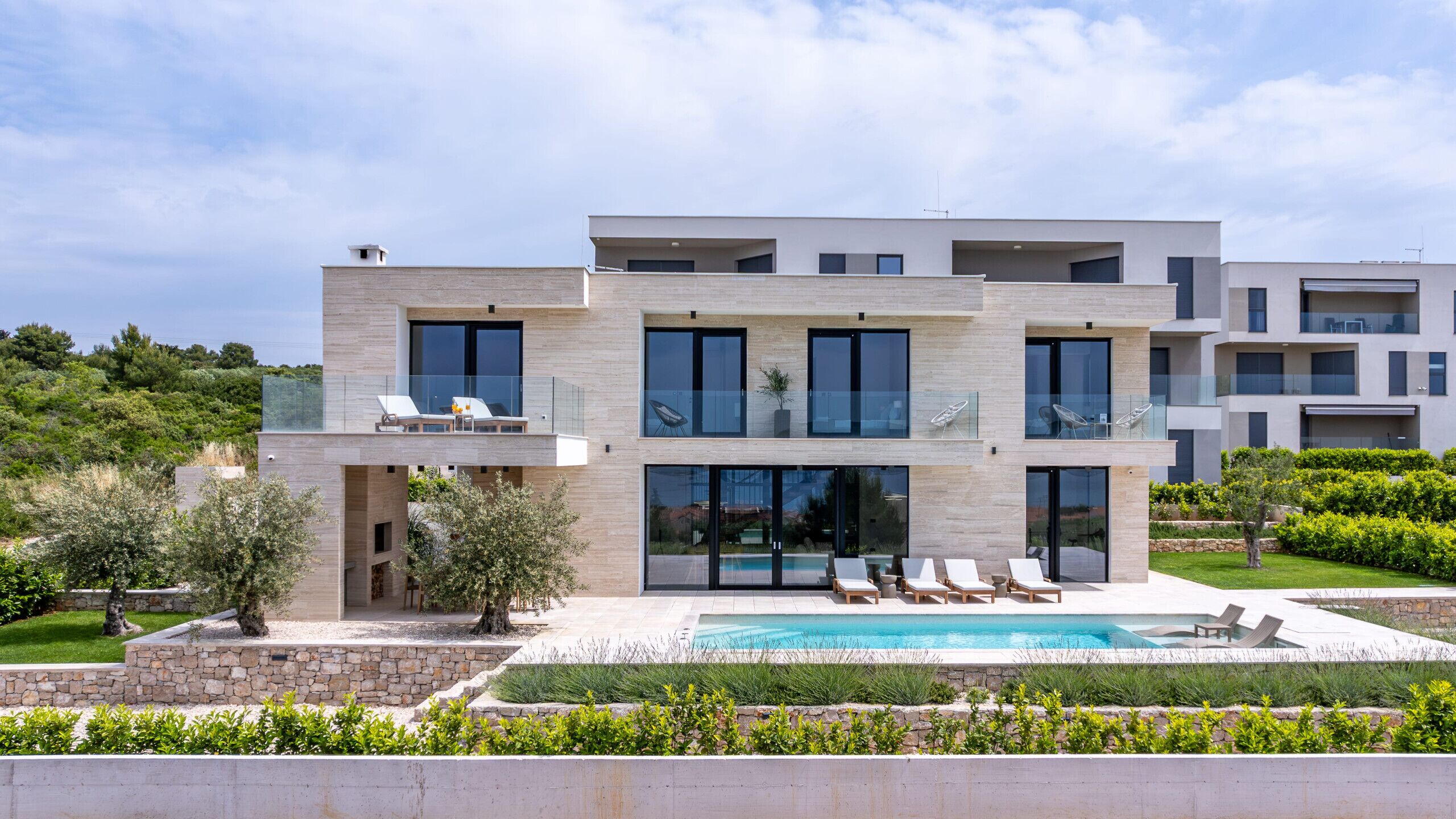 A modern multi-story house with a swimming pool, outdoor seating, and a well-maintained garden.