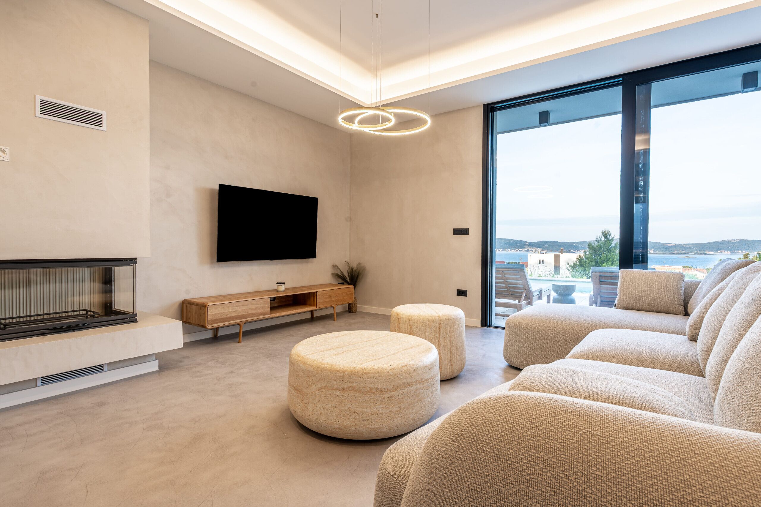 Ein modernes Wohnzimmer mit Flachbildfernseher, Kamin, Poufs und einem großen Fenster mit Blick auf die Stadt.