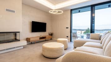 Ein modernes Wohnzimmer mit Flachbildfernseher, Kamin, Poufs und einem großen Fenster mit Blick auf die Stadt.