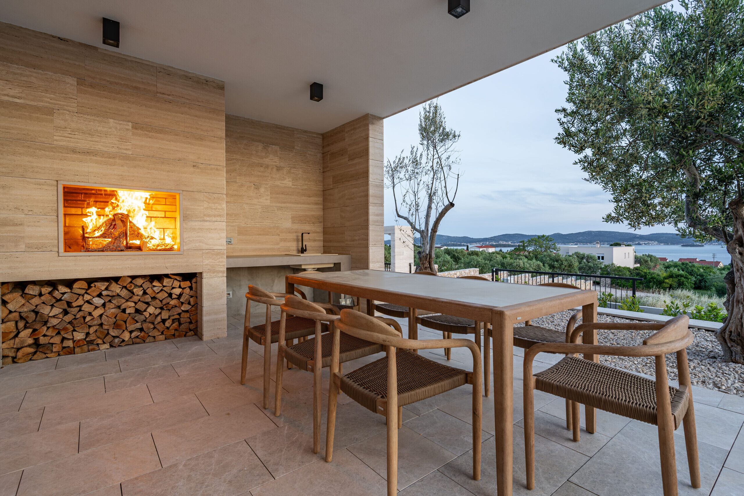 Eine Terrassenanlage im Freien mit Holztisch und -stühlen, einem eingebauten Kamin und Blick auf die Landschaft.