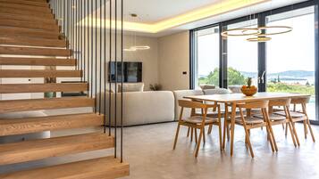 Ein modernes Interieur mit einer Holztreppe, einem Essbereich mit Holzsesseln und großen Fenstern mit Blick.