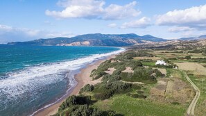 Paesaggio costiero con spiaggia, vegetazione e montagne sullo sfondo.