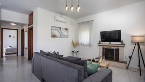 A modern living room with a sectional sofa, a flat-screen TV, a fireplace, and a floor lamp. - Casa Platoni (Apolakkia)
