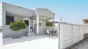 A modern house with a covered patio, a dining area with outdoor furniture, and a white fence. - Casa Platoni (Apolakkia)