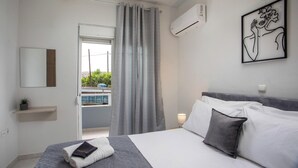 A modern bedroom with a bed, a bedside table, a wall-mounted air conditioner, and a window with curtains. - Casa Platoni (Apolakkia)