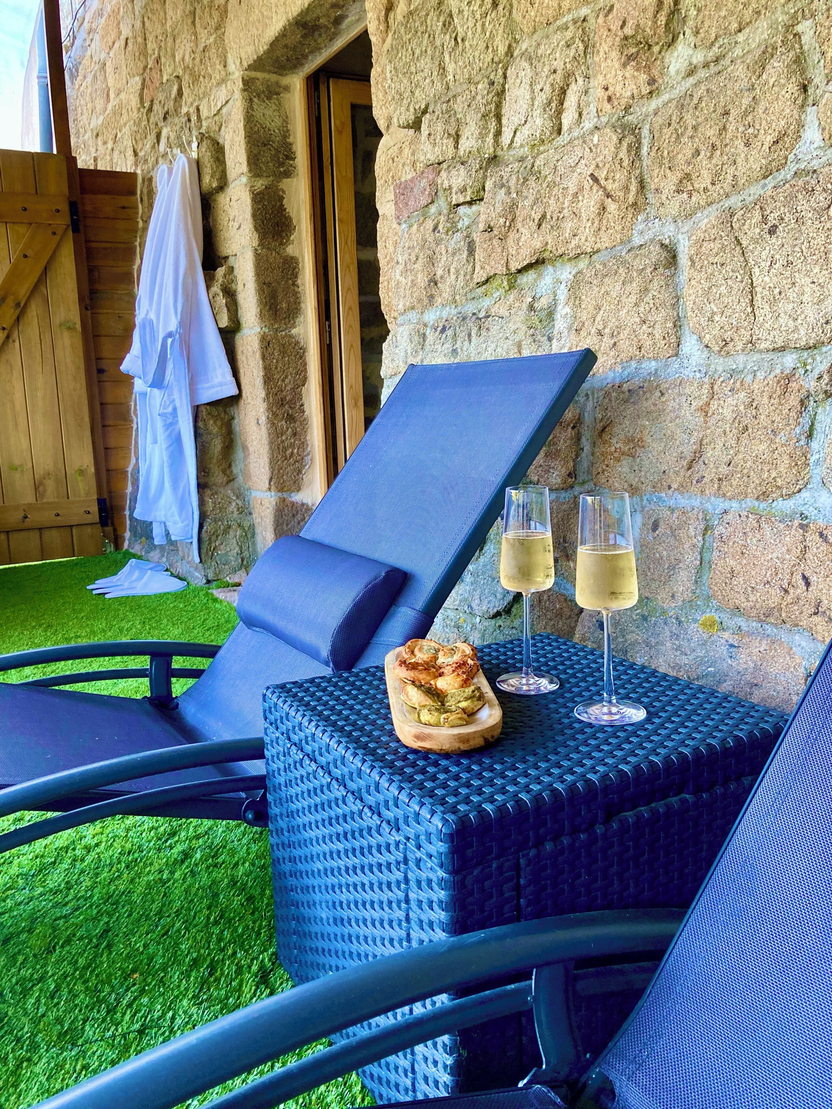 Un fauteuil confortable avec un coussin, une petite table avec une coupe de champagne et un plateau en bois contenant des aliments.