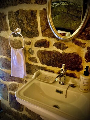 Une salle de bain avec un mur en pierre, un lavabo blanc, un miroir et une serviette suspendue à un anneau en métal.