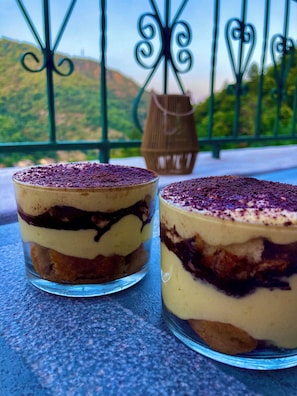 Deux coupes contenant un dessert à plusieurs couches sont posées sur une table. En arrière-plan, on aperçoit une clôture métallique et de la verdure.