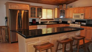 A kitchen with a stainless steel refrigerator, wooden cabinets, a black countertop, and a large island with stools.