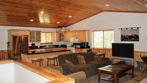A spacious living area with a wooden ceiling, a kitchen with wooden cabinets, a large flat-screen TV, and a cozy seating area with a coffee table.