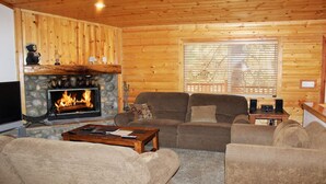 A cozy cabin interior with a stone fireplace, wooden walls, a comfortable sofa set, and a television.