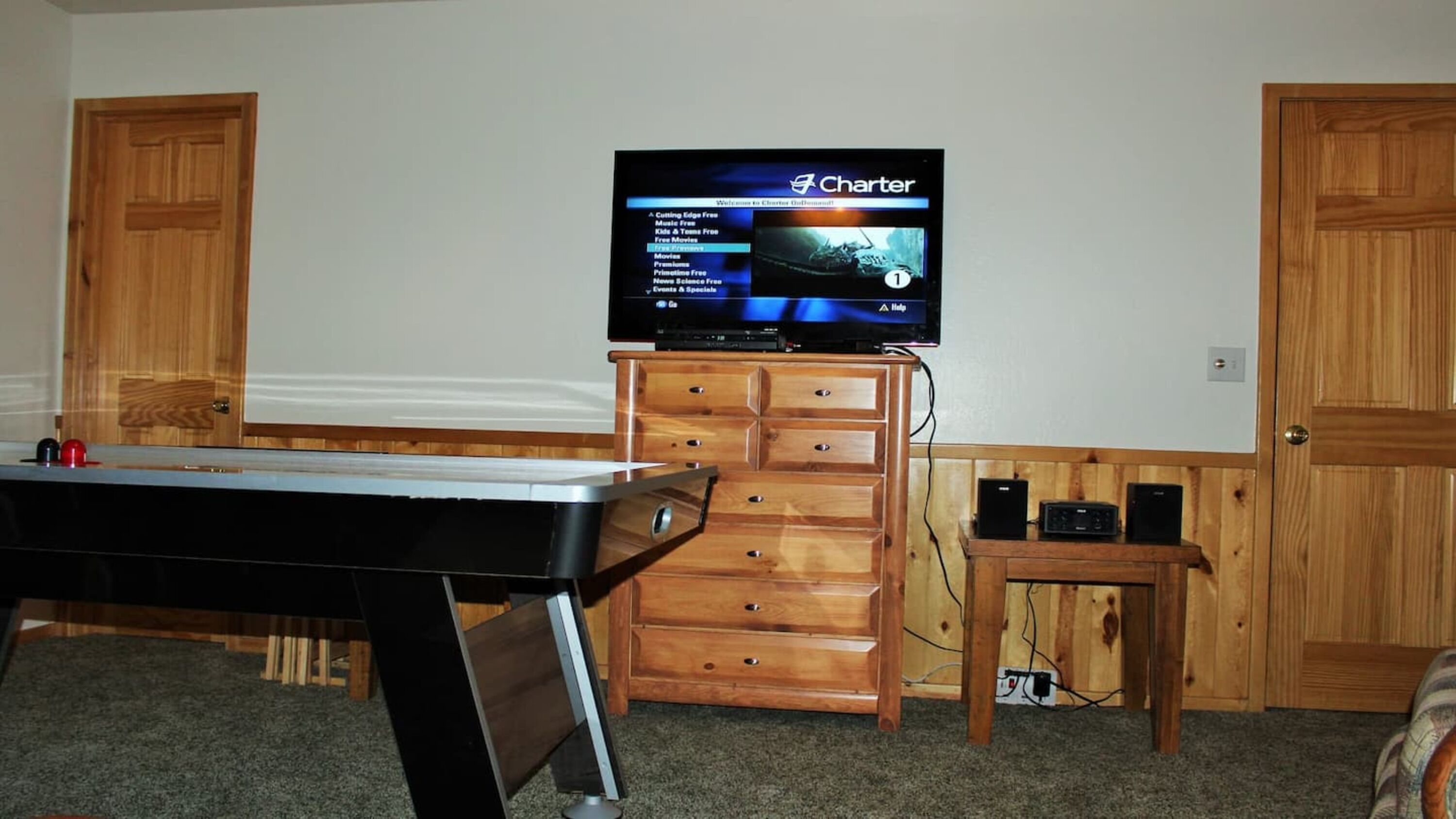 A room with a television on a wooden cabinet, a small table, and two doors.