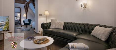 En moderne stue med en lædersofa, et sofabord og et fjernsyn. Der er en lysekrone på væggen og et maleri over sofaen.