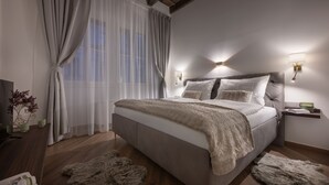 A bedroom with a large bed, wooden floor, fur rugs, a nightstand, and wall-mounted lamps. - Kaiserstein Palace Apartments (Prague)