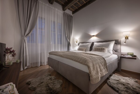A bedroom with a large bed, wooden floor, fur rugs, a nightstand, and wall-mounted lamps. - Kaiserstein Palace Apartments (Prague)