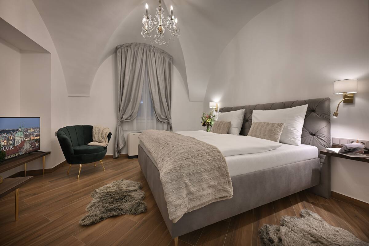 A modern bedroom with a large bed, a green armchair, a chandelier, and a cityscape view on the wall.