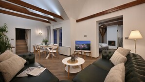 A modern living room with a sofa, a coffee table, and a TV. There is a staircase leading to another level, and a dining area with chairs and a table. - Kaiserstein Palace Apartments (Prague)