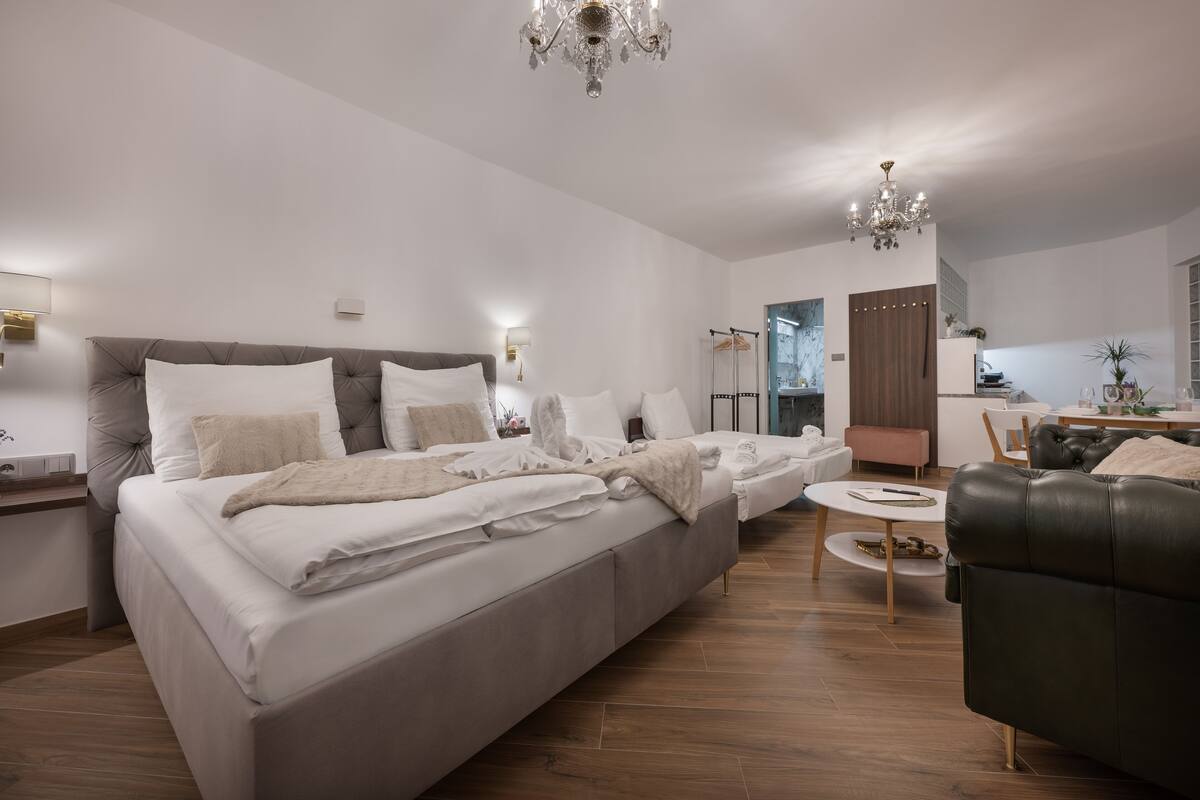 A modern bedroom with a large bed, bedside tables, a small seating area, and a dining table.