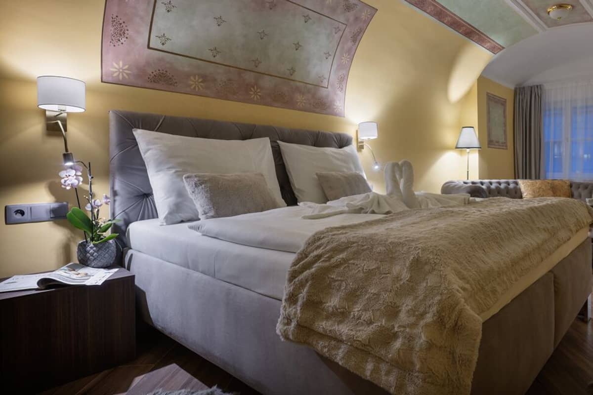 A well-appointed hotel room with a large bed, bedside lamps, a small table, and a potted plant.