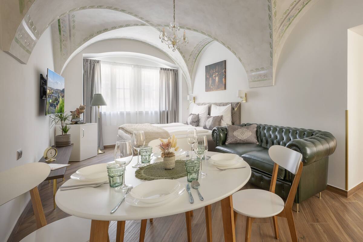 A dining area with a round table set for four, a green sofa, and a chandelier.