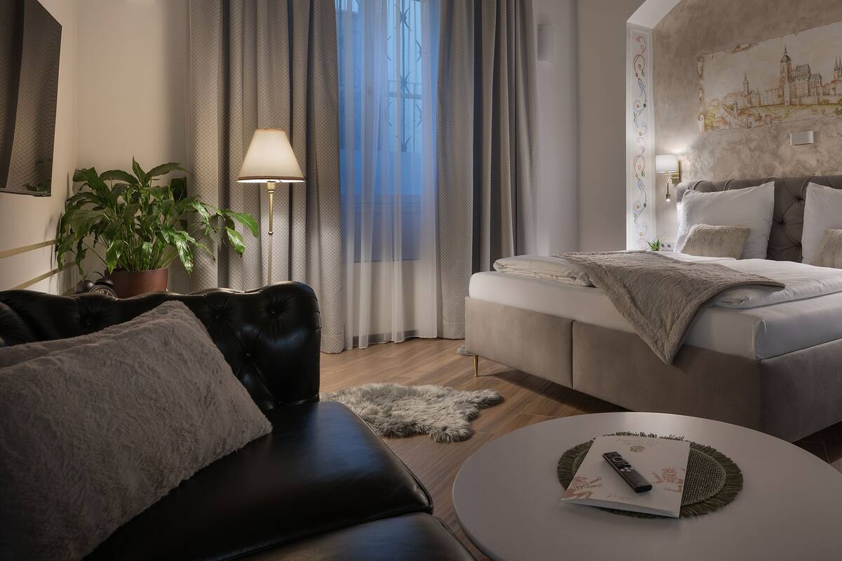 A modern hotel room with a large bed, a sofa, a dining table, and a potted plant.