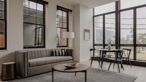 A modern living room with a sofa, a round coffee table, and a dining area with chairs and a table. - Sosuite One Bed Apt Accessible w Rooftop Gym Laundry (Philadelphia)