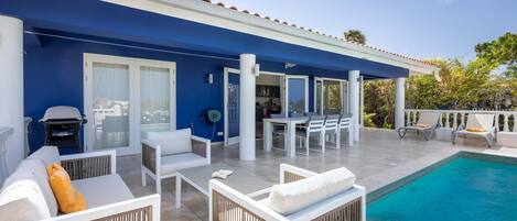 Un espace aménagé au bord de la piscine, avec des meubles blancs, un coin salon abrité et une vue sur la piscine.