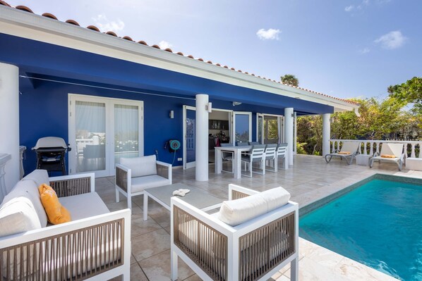 Un espace aménagé au bord de la piscine, avec des meubles blancs, un coin salon abrité et une vue sur la piscine.