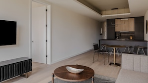 A modern living room with a round coffee table, a sofa, and a TV. There is a dining area with a table and chairs. The kitchen is visible in the background. - Sosuite One Bed Apt Plus w Rooftop, Gym, Laundry (Philadelphia)