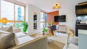 Een moderne woonkamer met een bank, eettafel en stoelen. Er is een televisie aan de muur en een keuken met kasten en een aanrecht.