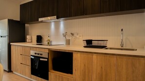 Eine moderne Küche mit dunklen Holzausziehtüren, einem Edelstahlkochfeld, einem eingebauten Backofen und einer weißen Arbeitsplatte.