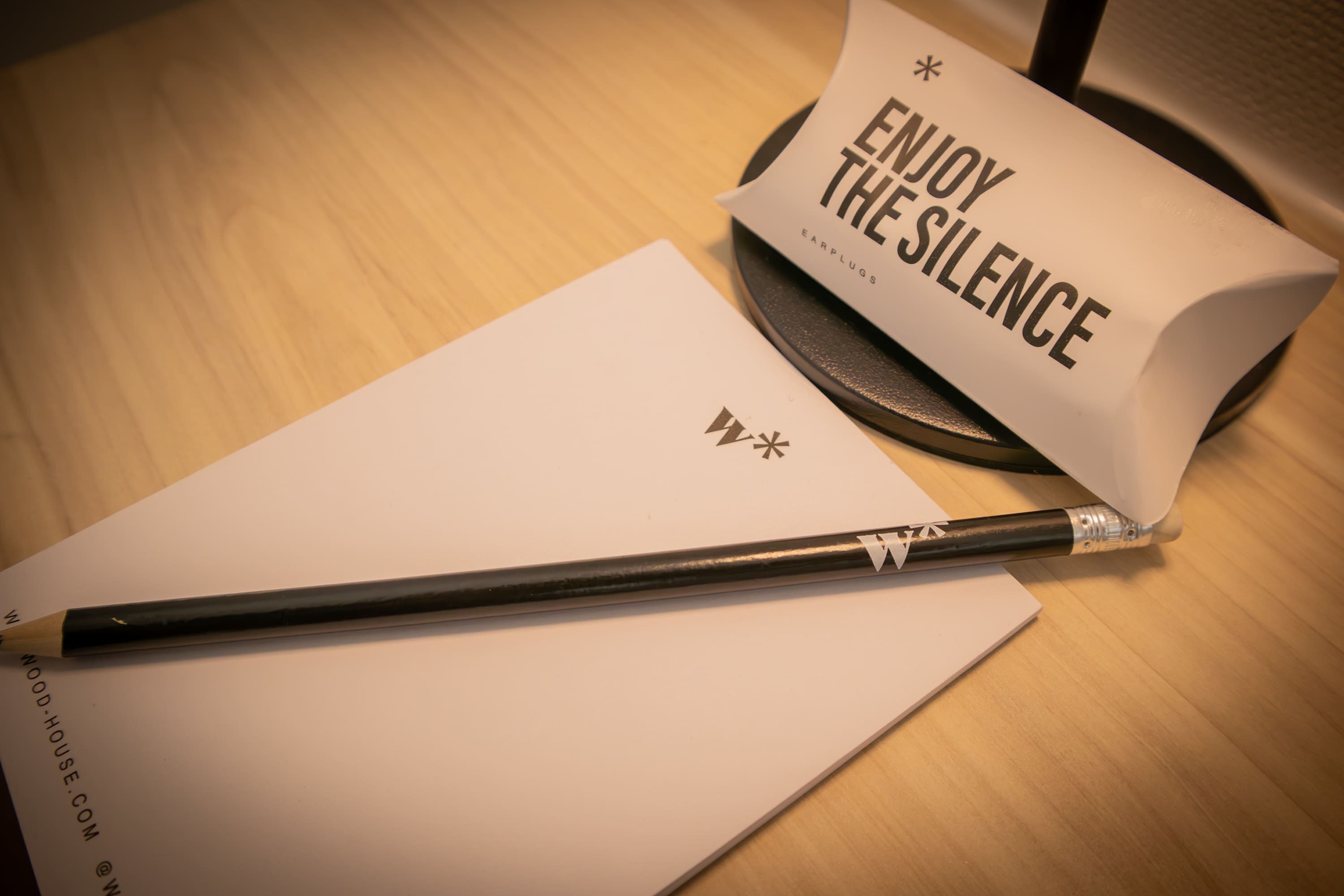 A desk with a white notepad, a black pencil, and a white envelope with the text "ENJOY THE SILENCE" on it.