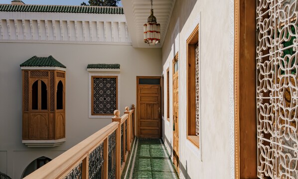 A narrow corridor with a wooden door, a window with intricate lattice, and a hanging lantern.