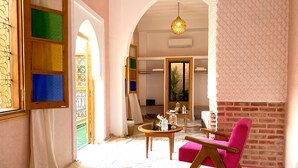 Une pièce avec une chaise rose, une table ronde en bois et un luminaire suspendu.