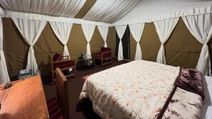 A tent-style room with a bed, two chairs, a table, and a lamp. - Camp OM Riverside Retreat (Pokhri)