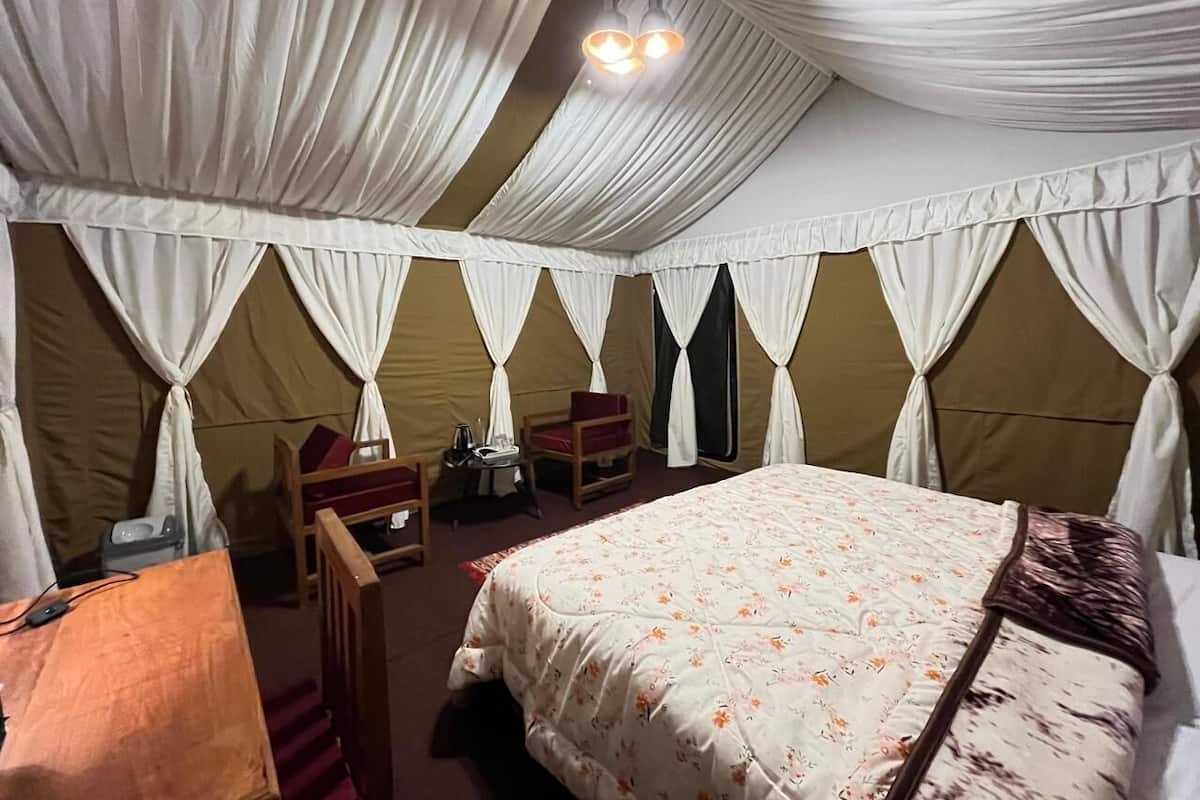 Quarto tipo tenda com cama, duas cadeiras, uma mesa e um abajur.