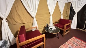 A tented room with two wooden chairs, a small table with a kettle, and a colorful rug. - Camp OM Riverside Retreat (Pokhri)