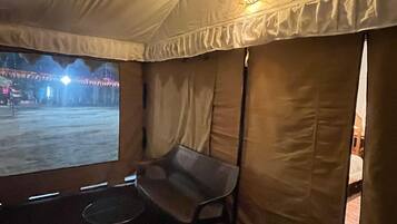 A tented room with a bench, a small table, and a view of an outdoor area with lights.